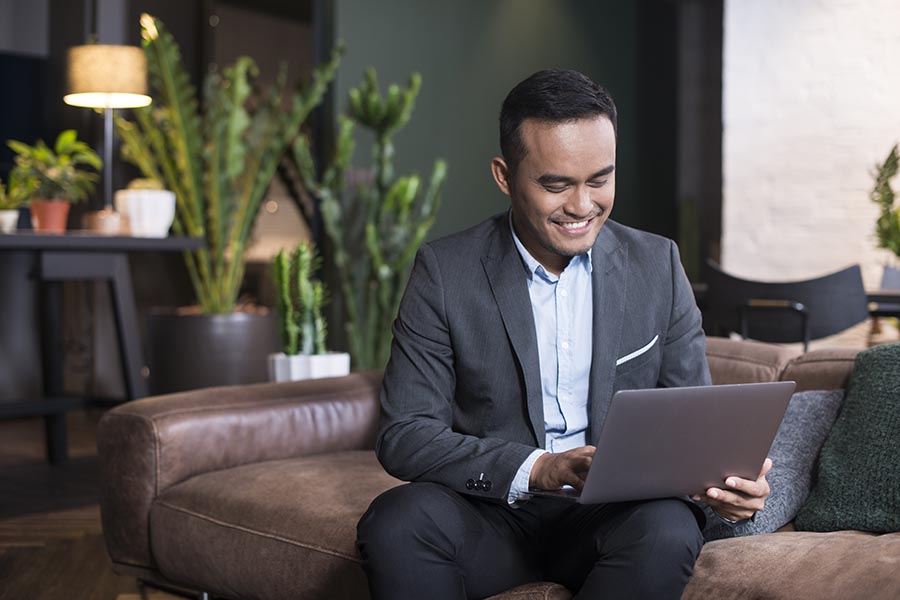 Blog - Businessman Uses a Computer on a Leather Couch in an Office Lobby, Potted Cacti Behind Him