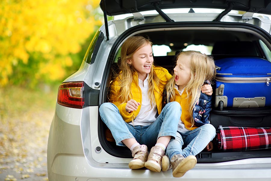 Contact Us - Kids Sitting in the Back of a Car, Ready for a Road Trip, Bags Packed in the Trunk