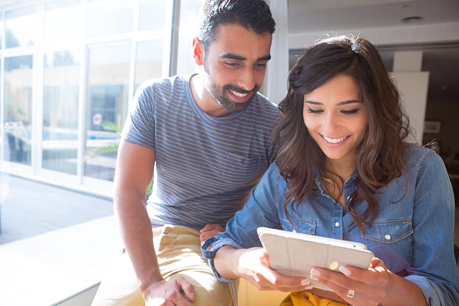 Get a Quote - Couple Using a Tablet, Smiling and Sitting Close by a Large Window